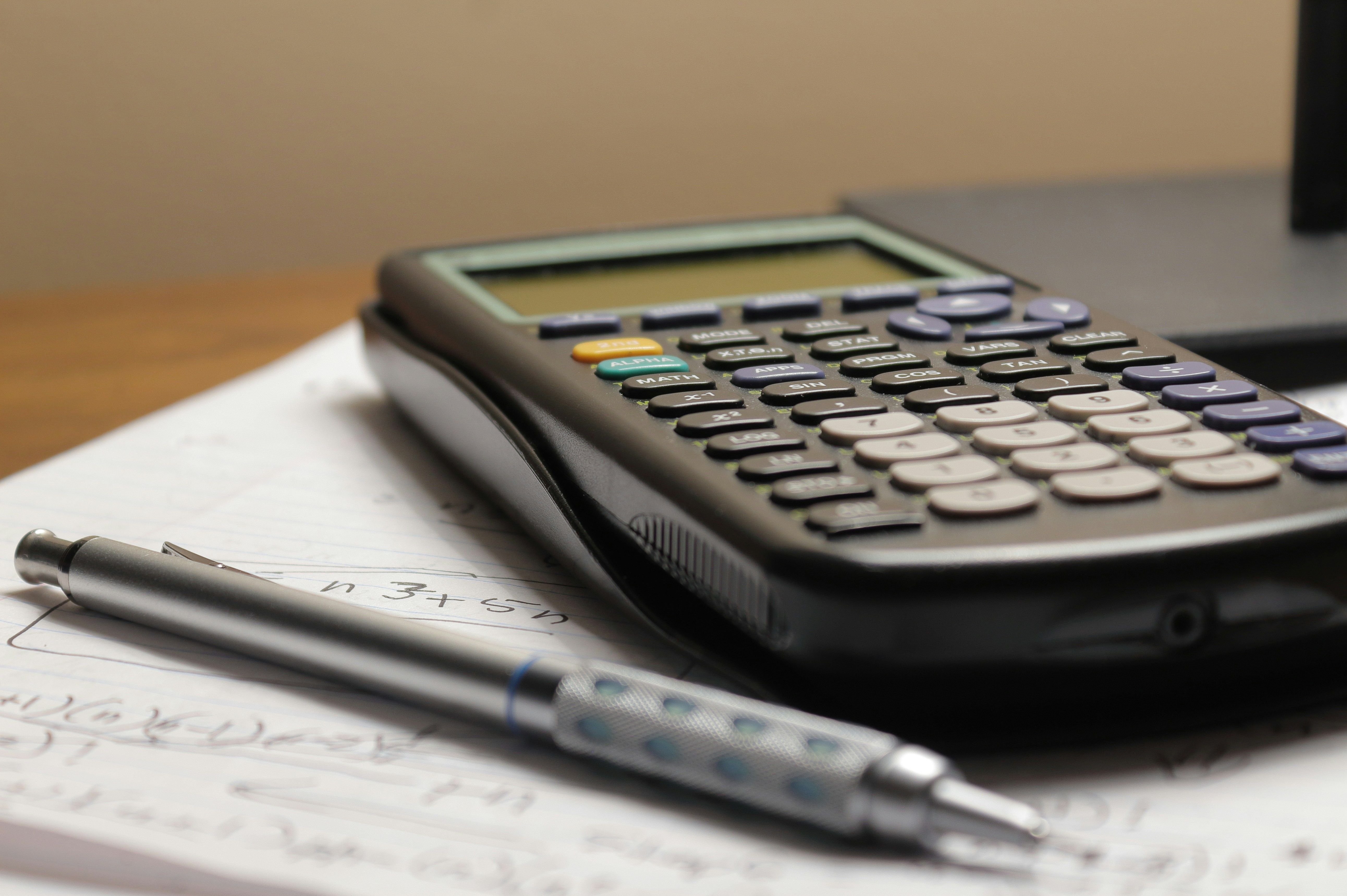 A calculator and pen on top of a notepad