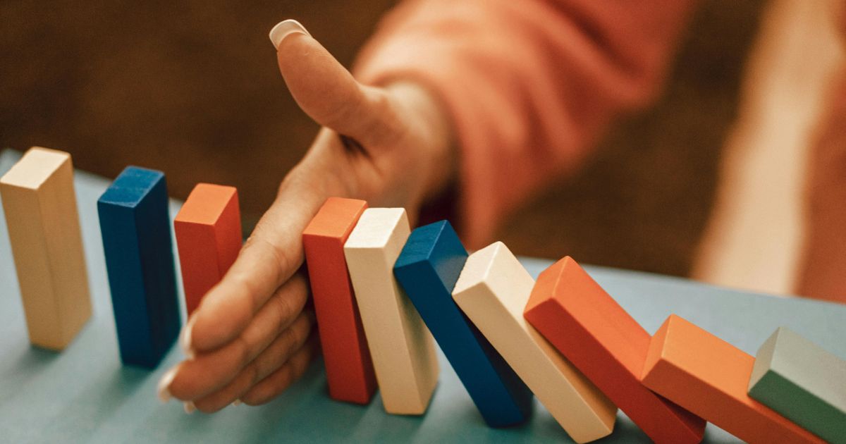Hand of a woman blocking falling dominos