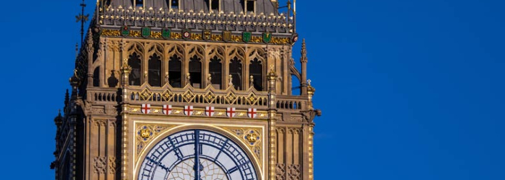 A close-up of the clock face of Big Ben Clock Tower with a blue sky in the background
